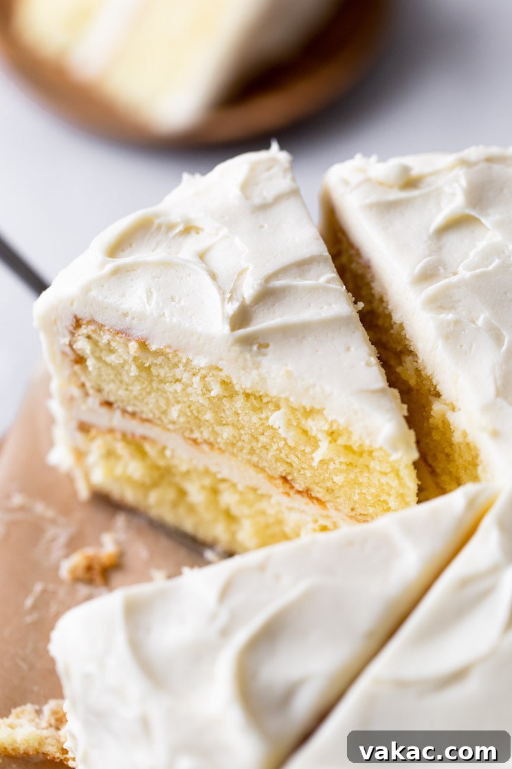 An inviting overhead shot of a beautifully sliced vanilla cake featuring generous layers of creamy vanilla buttercream. One perfect slice has already been neatly removed, tempting anyone nearby.