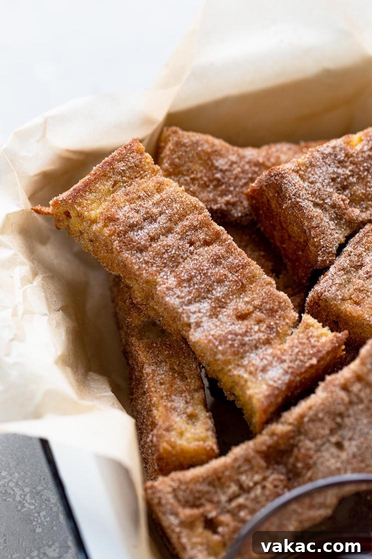 A pile of cinnamon french toast sticks in a baking dish lined with parchment paper.