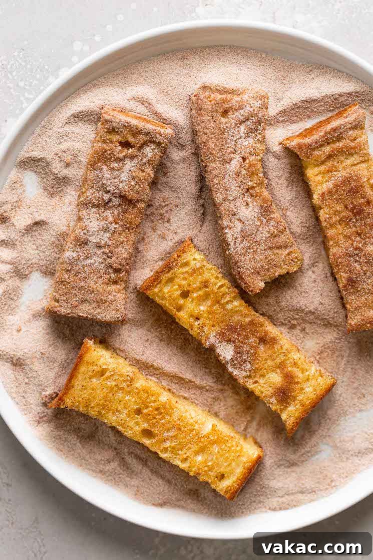 Cinnamon french toast sticks being rolled in cinnamon sugar, viewed from above.