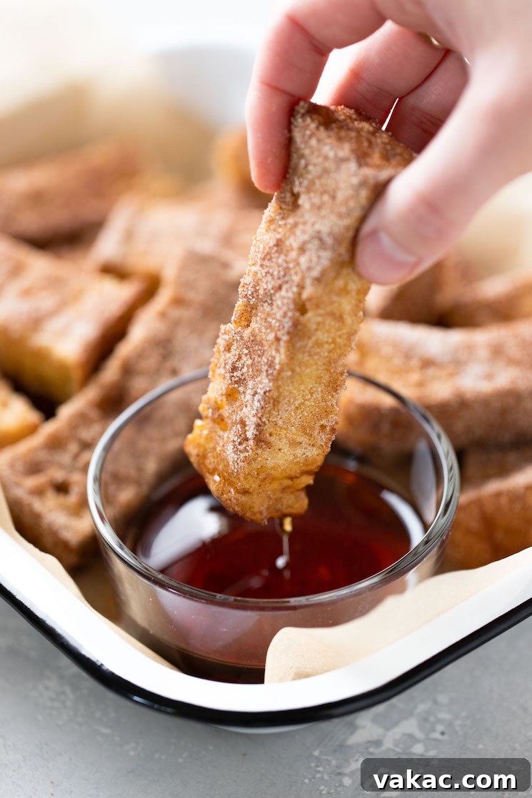 A baked french toast stick being dunked into a small dish of maple syrup.