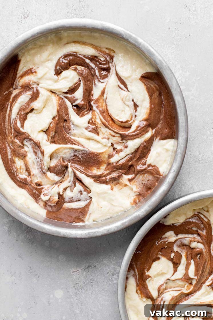 An overhead view of swirled marble cake batter in two cake pans, ready to be baked.