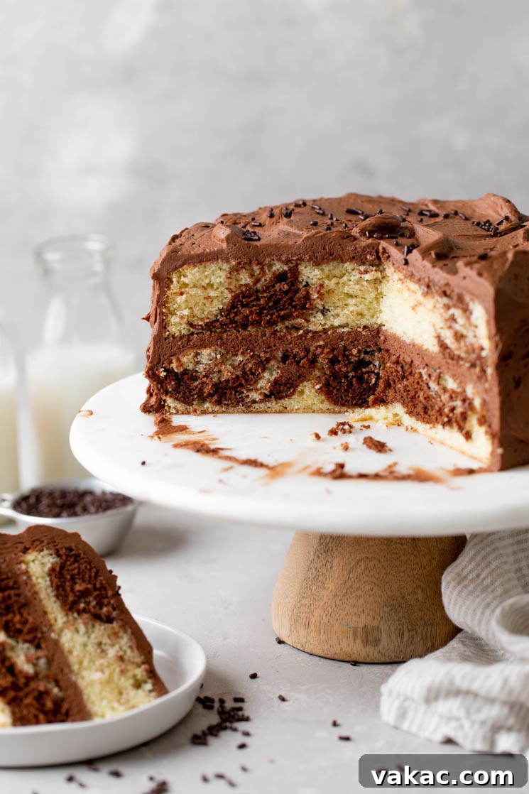 Marbled Perfection 8 A side view of a homemade marble cake on a cake stand. A slice has been removed and has been plated. Milk jugs rest in the background.