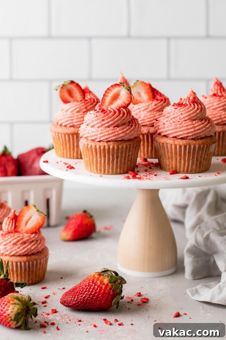 Luscious Strawberry Cupcakes 2 A side view of fresh strawberry cupcakes on a cake stand. Additional cupcakes and fresh berries litter the counter underneath.