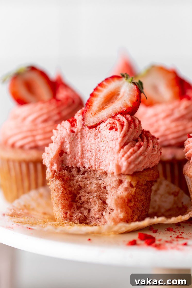 Luscious Strawberry Cupcakes 8 A close up view of cupcakes with strawberry frosting on a cake stand. The front cupcake has a bite missing.