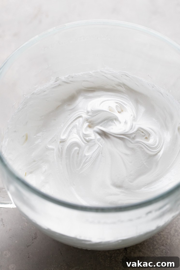Velvet Meringue Frosting 5 An overhead view of egg whites that have been whipped to stiff peaks in a glass mixing bowl.