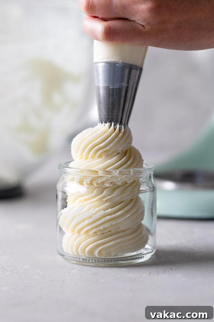 Velvet Meringue Frosting 7 Swiss meringue buttercream being piped into a glass jar from a piping bag.