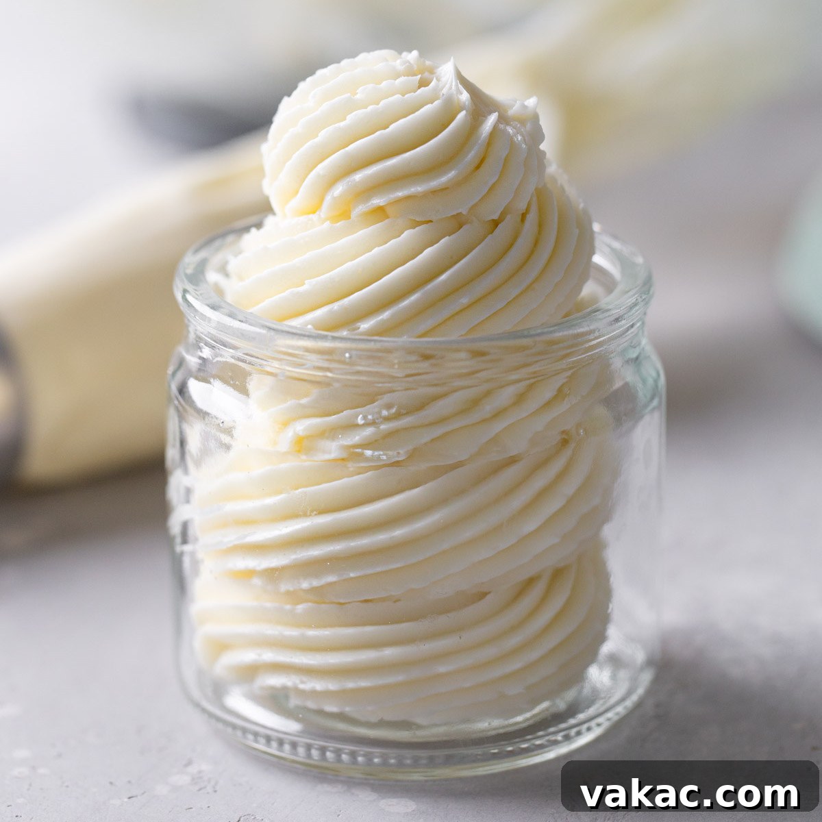 Swiss meringue buttercream frosting piped into a glass jar. A piping bag lies in the background.