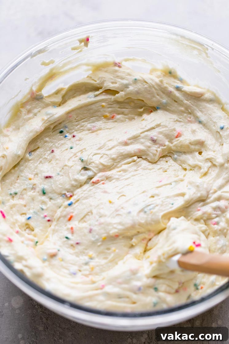 Rainbow Sprinkle Delight 4 An overhead view of funfetti cake batter in a glass mixing bowl with a rubber spatula.