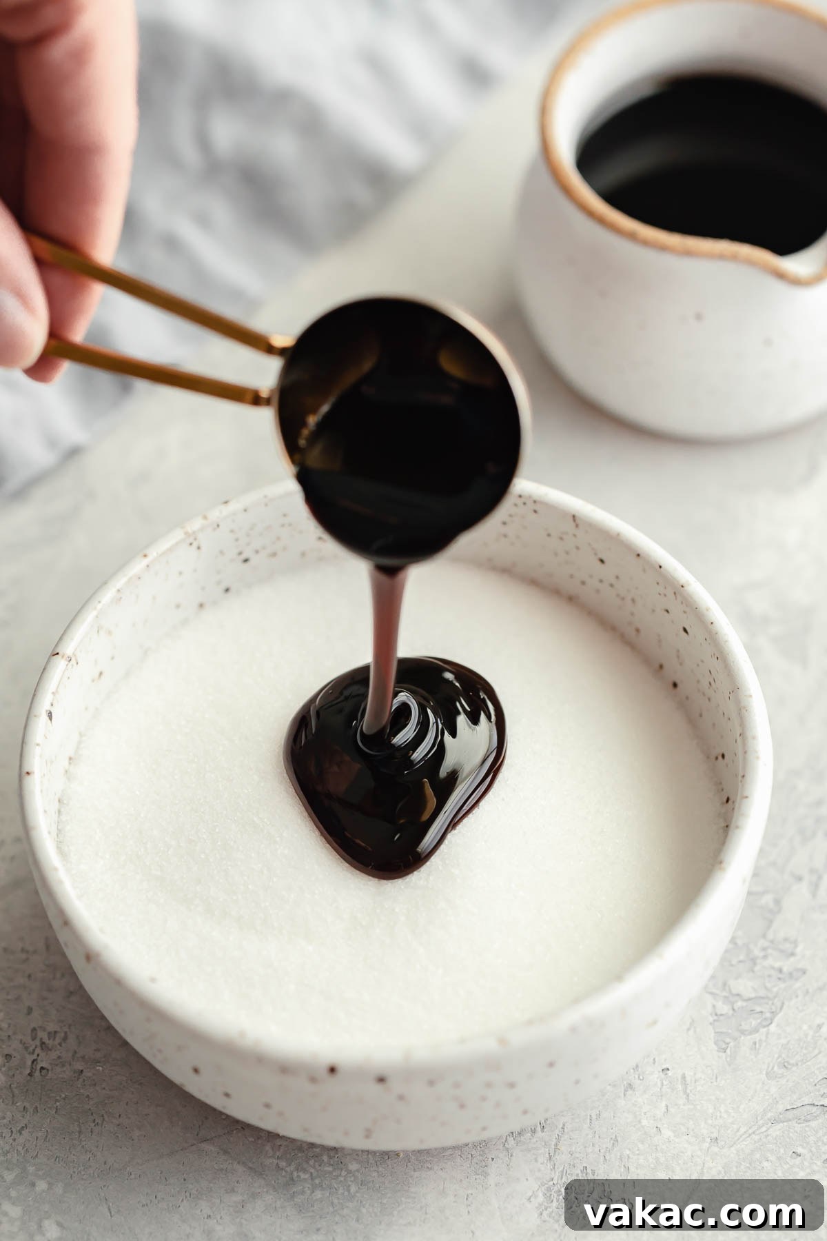 Molasses being carefully poured into a bowl of granulated sugar, with a jug of molasses in the background.