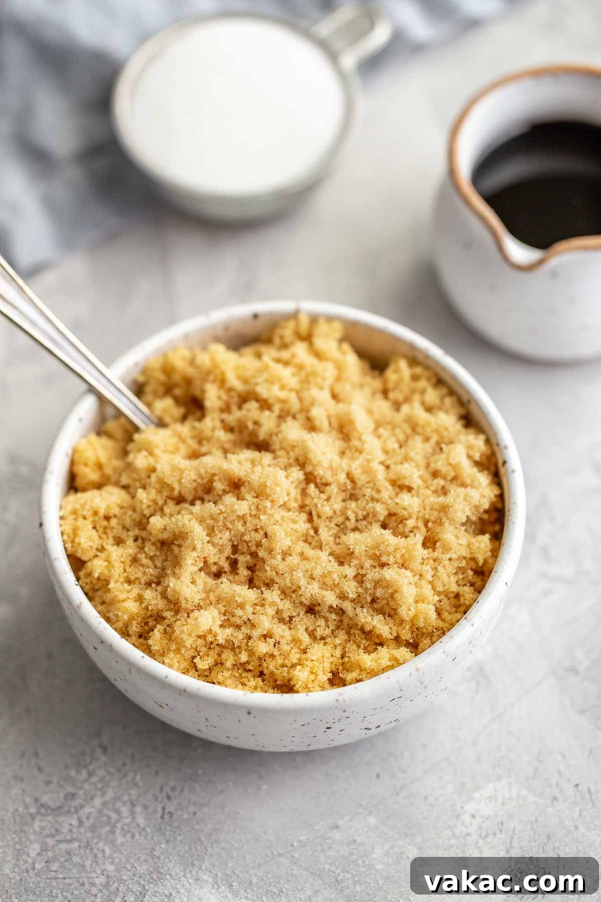 A bowl of homemade brown sugar with a spoon sticking out, next to a small jug of molasses, showing the finished product.
