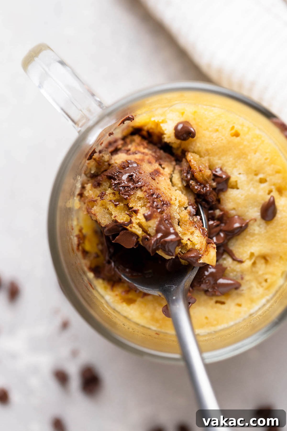 Chocolate Chip Mug Treat 6 An overhead shot captures a spoon expertly digging into the soft, warm center of a freshly microwaved mug cookie, revealing its gooey texture.