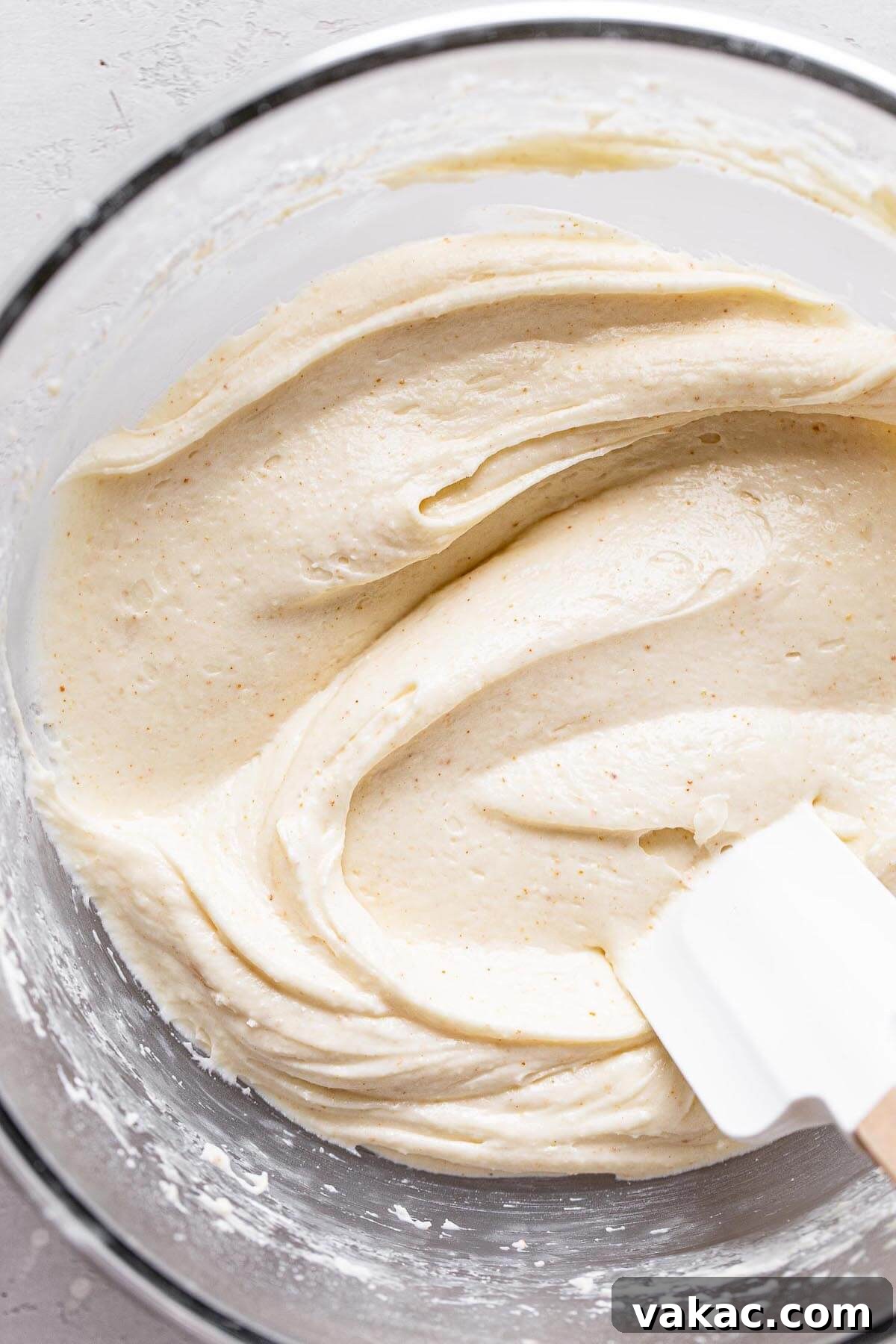 Sweet Banana Bites 5 An overhead view of a glass mixing bowl full of brown butter cream cheese frosting. A rubber spatula rests in the bowl.