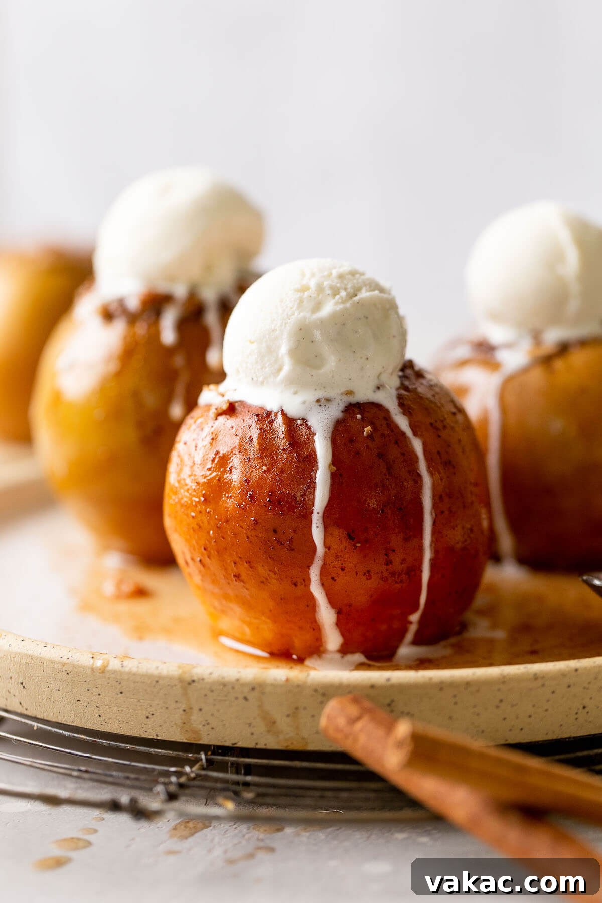 Warm Spiced Apple Bake 2 Three stuffed baked apples topped with vanilla ice cream on a speckled white plate.