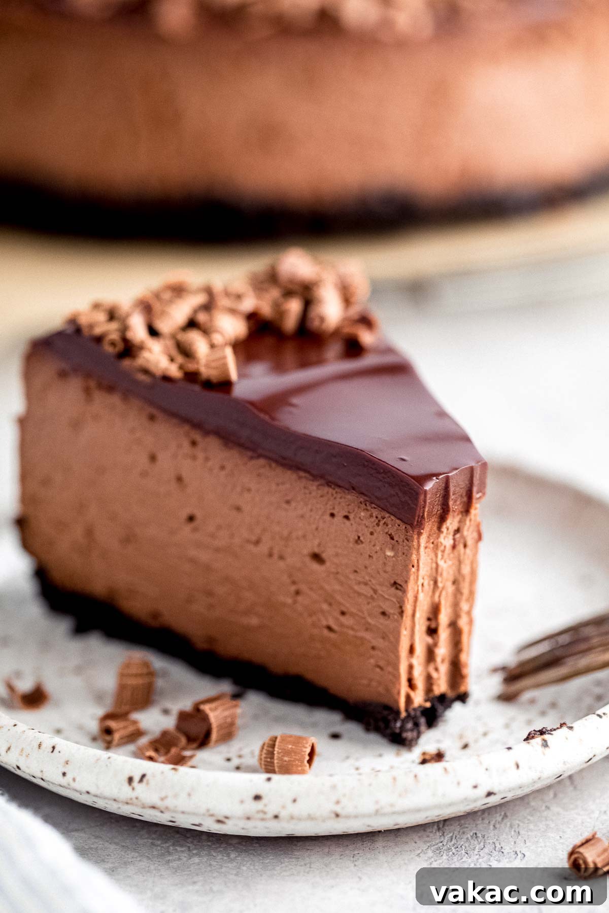 A slice of rich chocolate cheesecake with a small bite missing, served on a stylish white speckled plate, highlighting the dense and creamy texture.