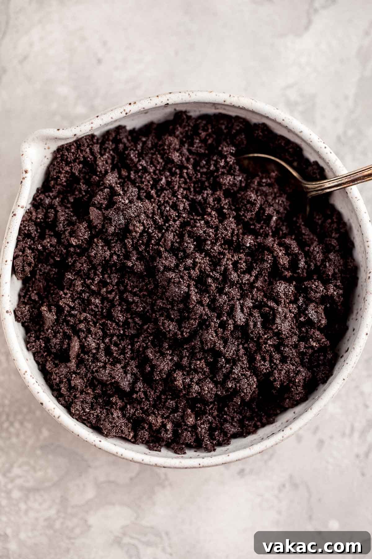 An overhead view of finely crushed Oreos in a large white mixing bowl, ready to be combined with butter for the cheesecake crust.