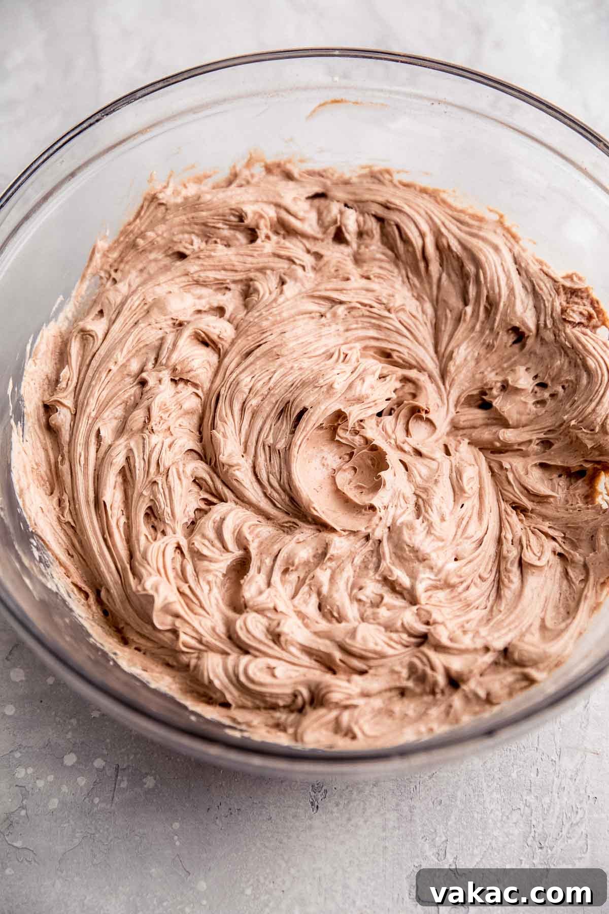 An overhead view of the initial stage of chocolate cheesecake filling in a glass mixing bowl, showcasing its rich, dark color and smooth consistency.