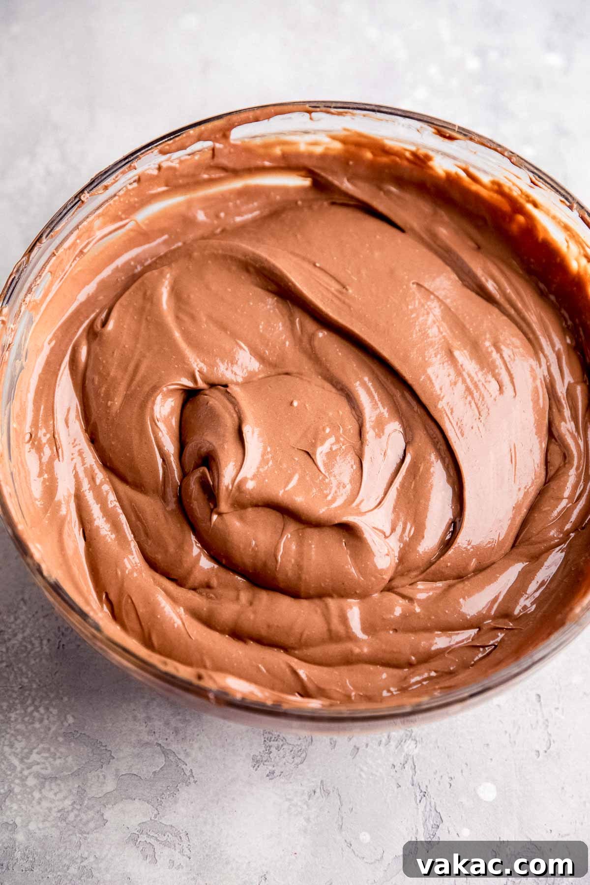 An overhead view of a smooth, perfectly blended chocolate cheesecake filling in a clear glass mixing bowl, illustrating the creamy texture achieved before baking.