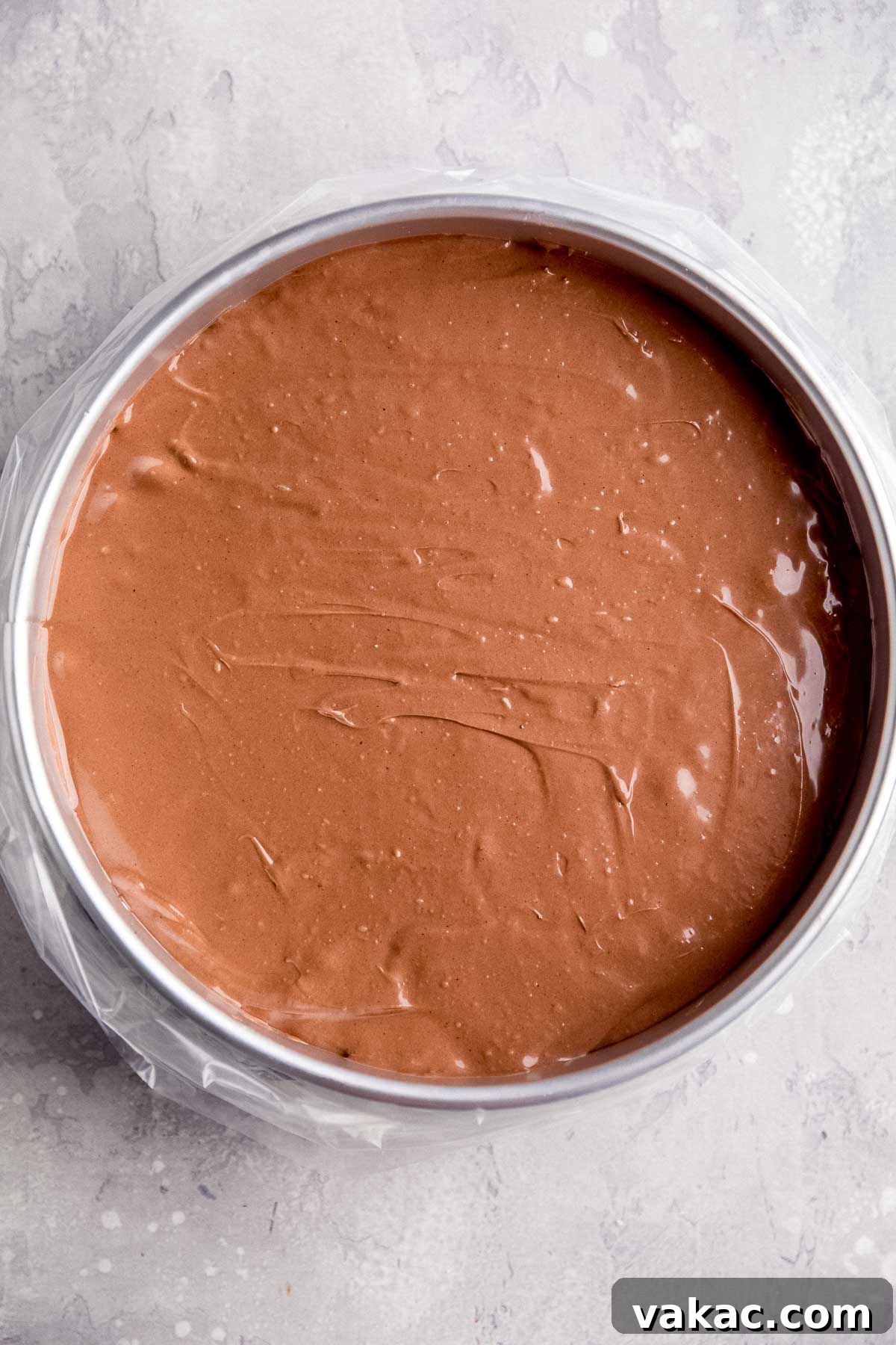 An overhead view of an unbaked chocolate cheesecake nestled in a springform pan, meticulously placed inside an oven bag, highlighting the preparation for a water bath to ensure a perfectly baked, crack-free dessert.