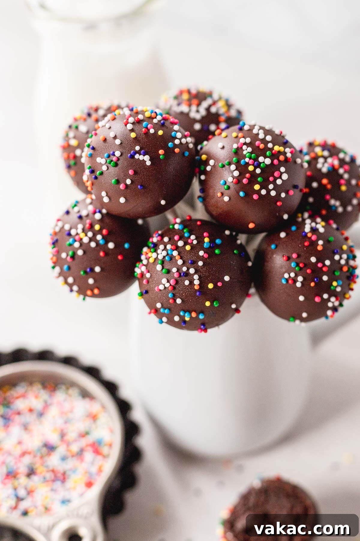 Ultimate Homemade Chocolate Cake Pops 2 A bouquet of chocolate cake pops in a white vase. Sprinkles rest in the foreground.