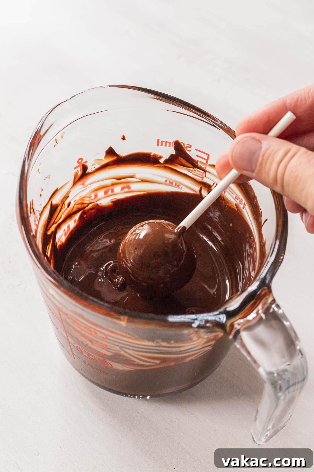 A cake pop being dunked into a glass of melted chocolate.