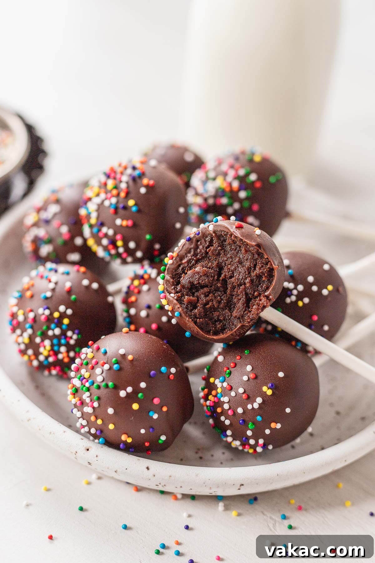 Ultimate Homemade Chocolate Cake Pops 9 Chocolate cake pops piled on a white speckled plate. One cake pop has a bite missing.