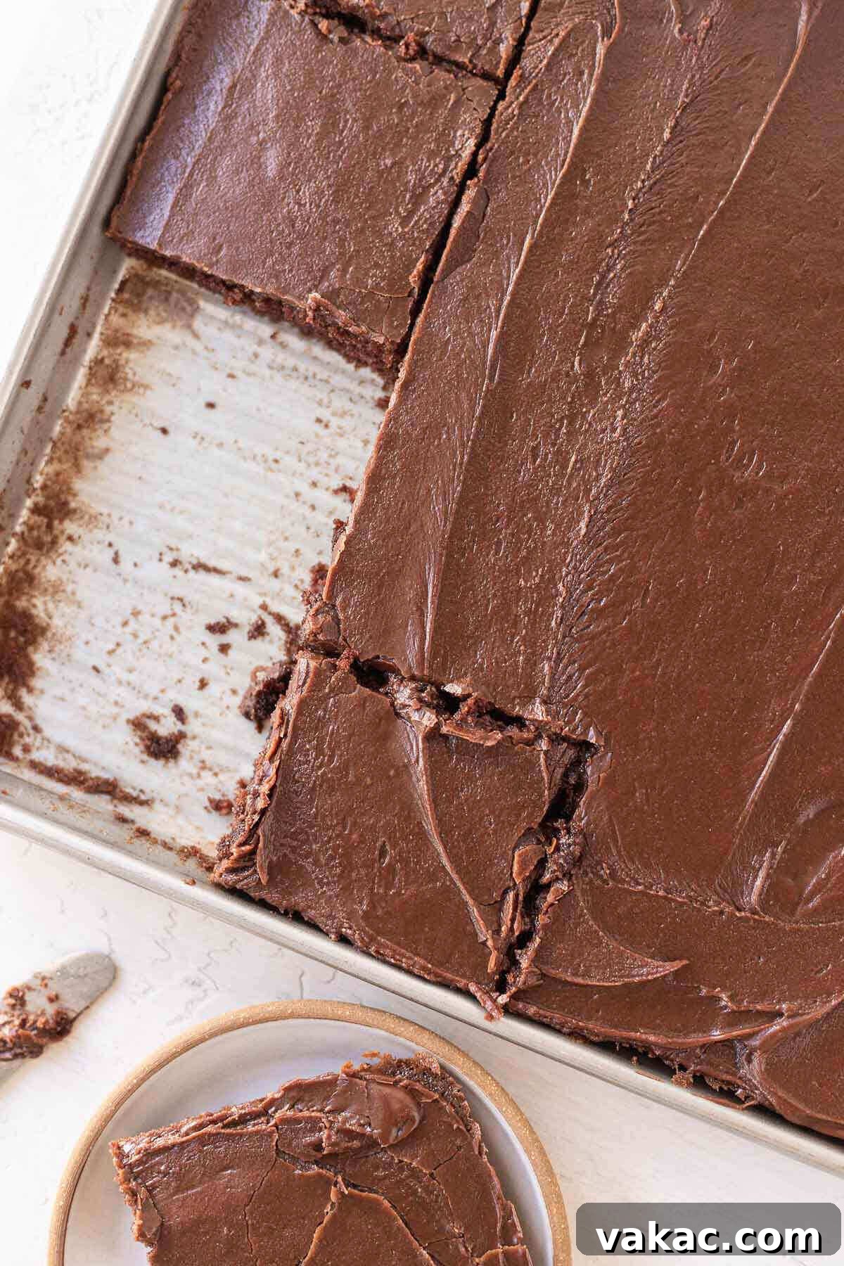 Ultimate Texas Sheet Cake 7 An overhead view of a freshly baked Texas sheet cake in its rectangular pan. The cake has been neatly sliced into squares, and one slice has been removed, revealing the tender, dark crumb.