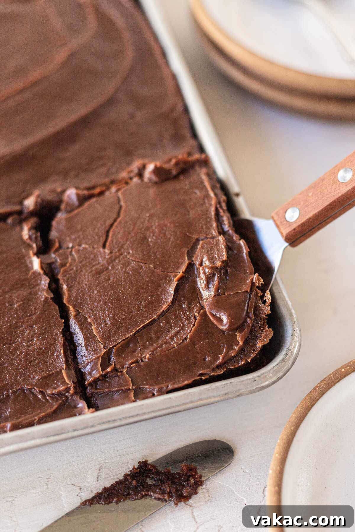 Ultimate Texas Sheet Cake 8 A slice of Texas sheet cake being carefully removed from the pan with a spatula, highlighting its thin yet substantial layer and rich, dark frosting.