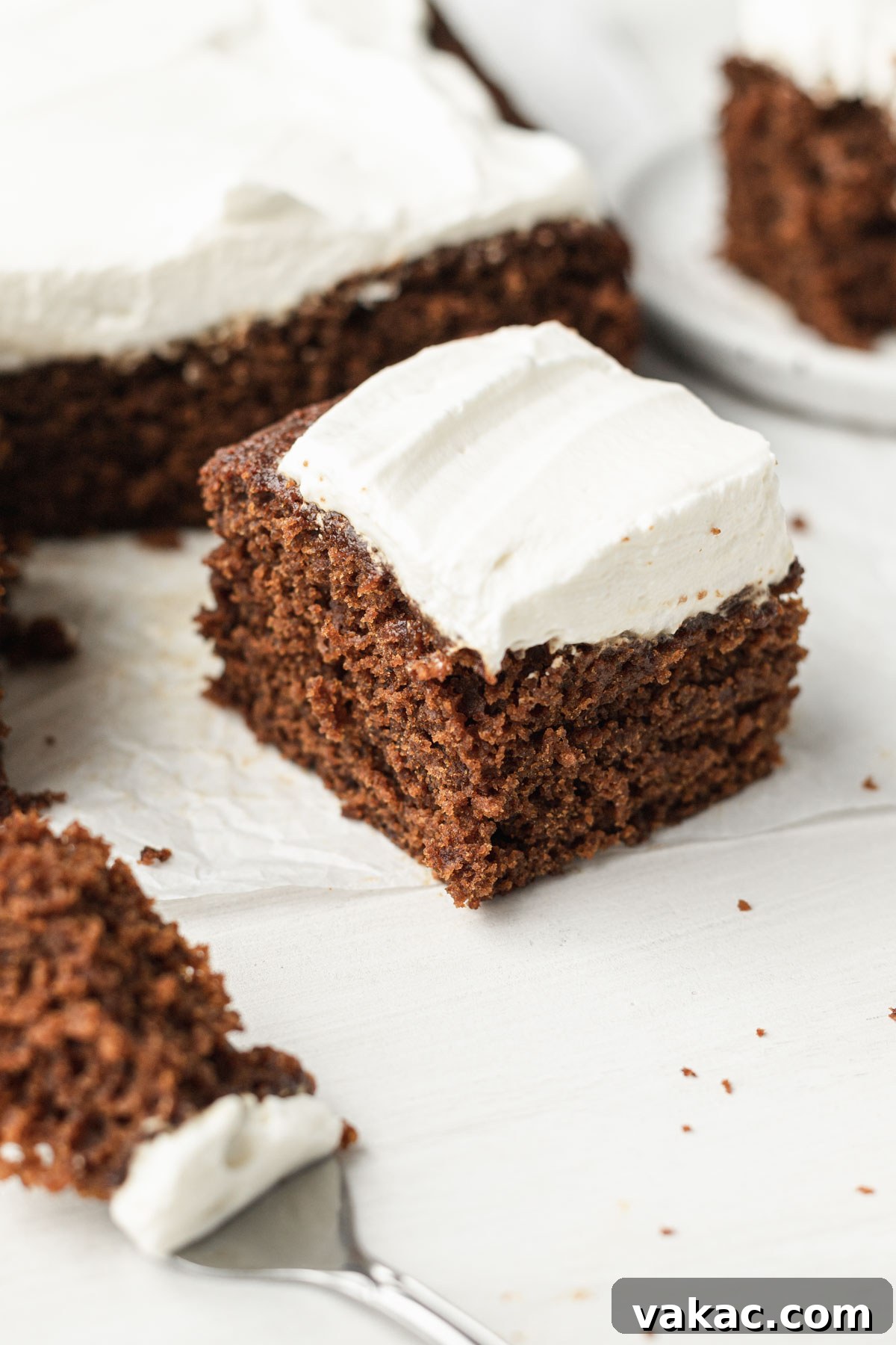 A slice of gingerbread cake topped with whipped cream, with the rest of the cake in the background.