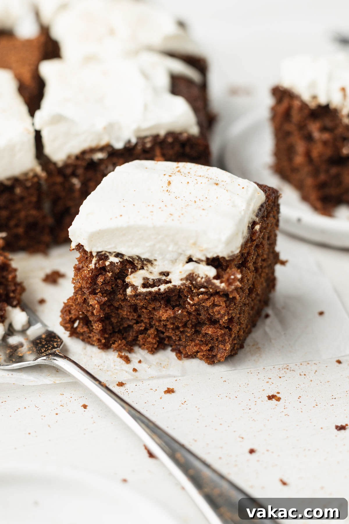 Slices of spiced molasses cake topped with whipped cream, with a fork resting beside them.
