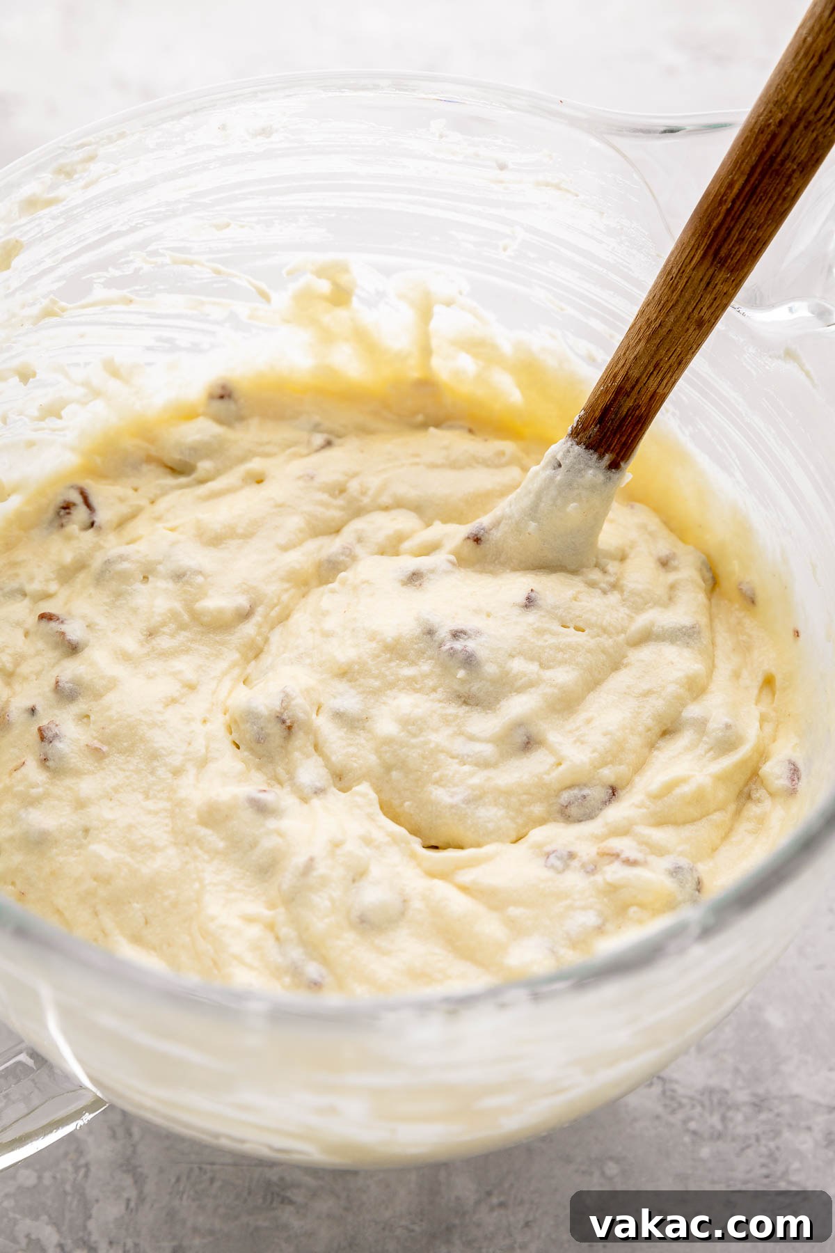 Velvet Italian Cream Indulgence 7 A large glass mixing bowl holds a luxurious Italian Cream Cake batter, enriched with gently folded-in whipped egg whites, scattered with crunchy pecans and sweet shredded coconut, showcasing a light and airy texture ready for baking.