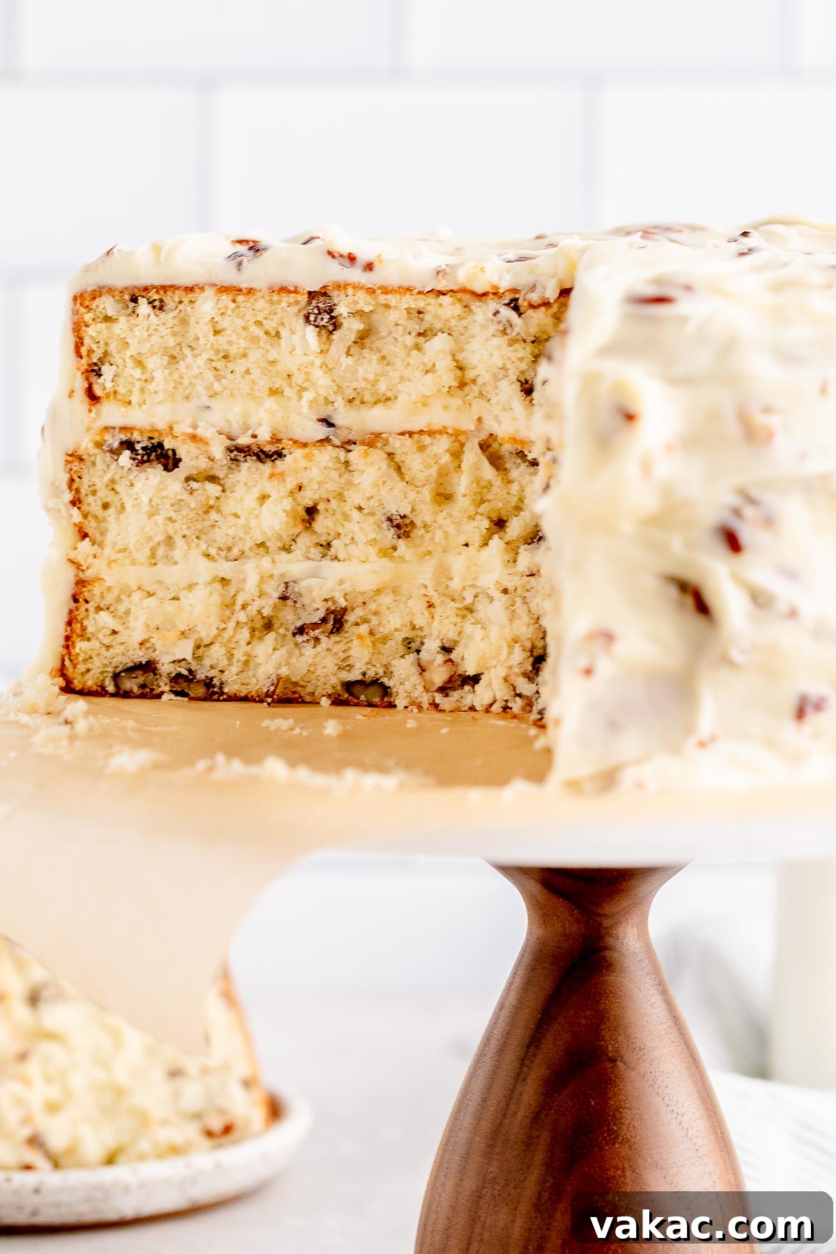 Velvet Italian Cream Indulgence 9 A close-up shot of a perfectly sliced Italian Cream Cake, revealing its delicate, moist crumb texture with visible pieces of toasted pecans and shredded coconut embedded within. A full slice of the cake and a jug of milk are softly blurred in the background, emphasizing the cake's appealing cross-section.