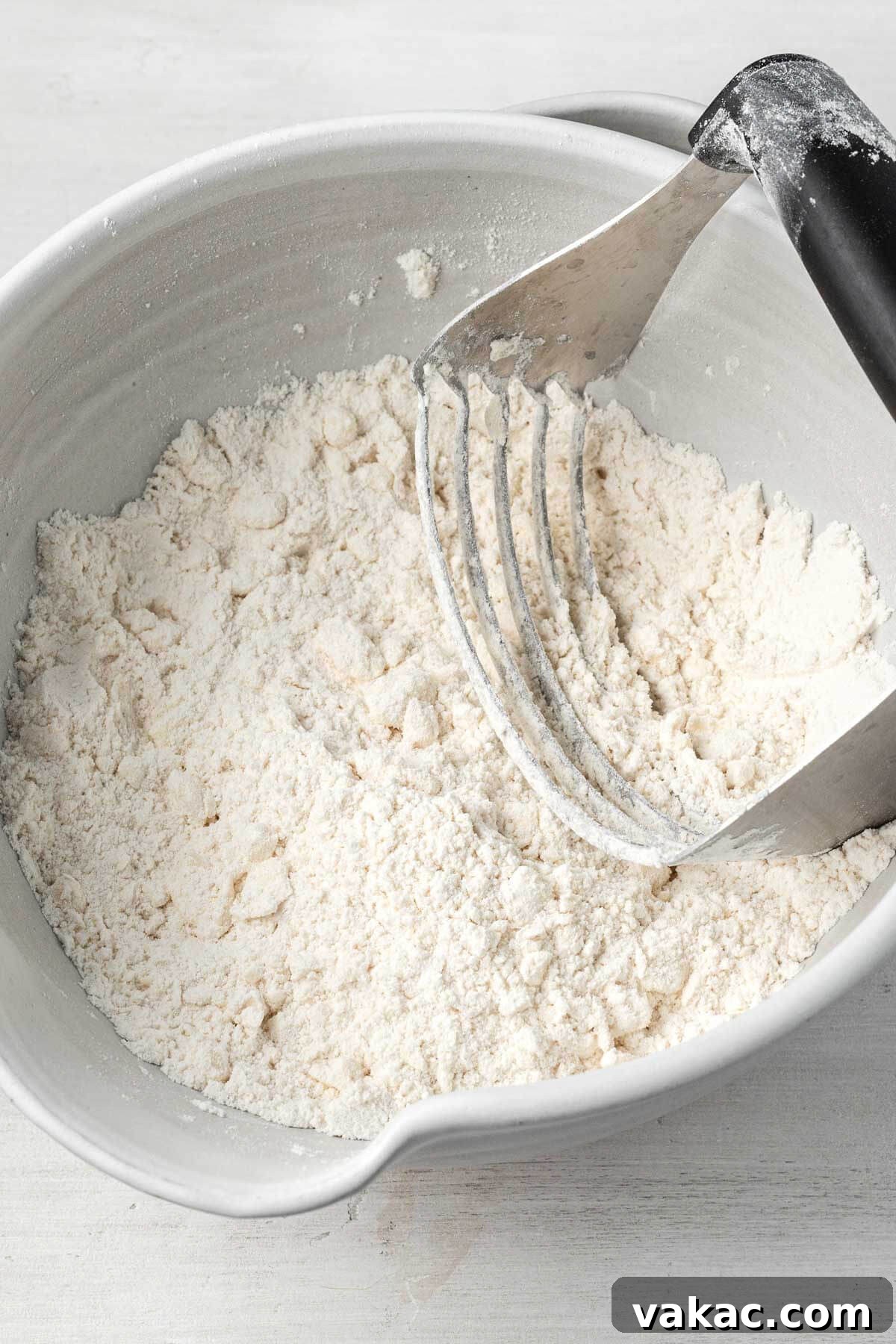 An overhead view of cold butter being cut into a flour mixture using a pastry cutter, crucial for flaky biscuits.