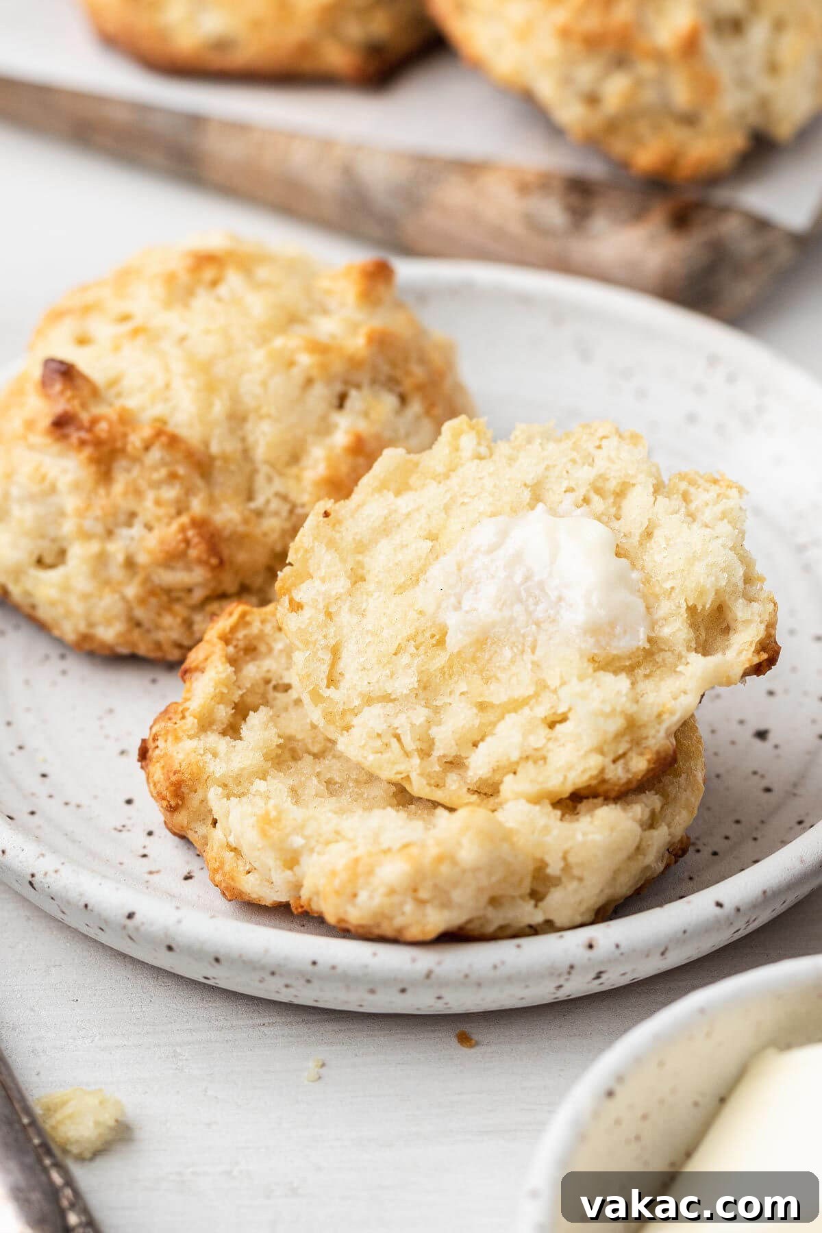 Easy Homemade Drop Biscuits 6 Two drop biscuits on a white plate. One biscuit has been cut in half and topped with a pat of melting butter, highlighting its soft interior.