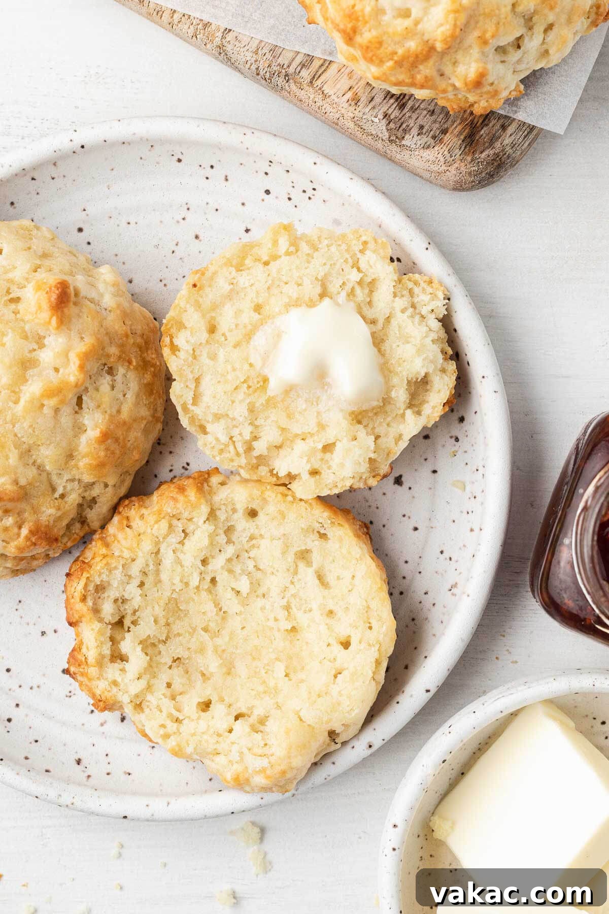 Easy Homemade Drop Biscuits 7 An overhead view of several homemade drop biscuits on a white plate, one halved and topped with butter, showcasing the internal texture.