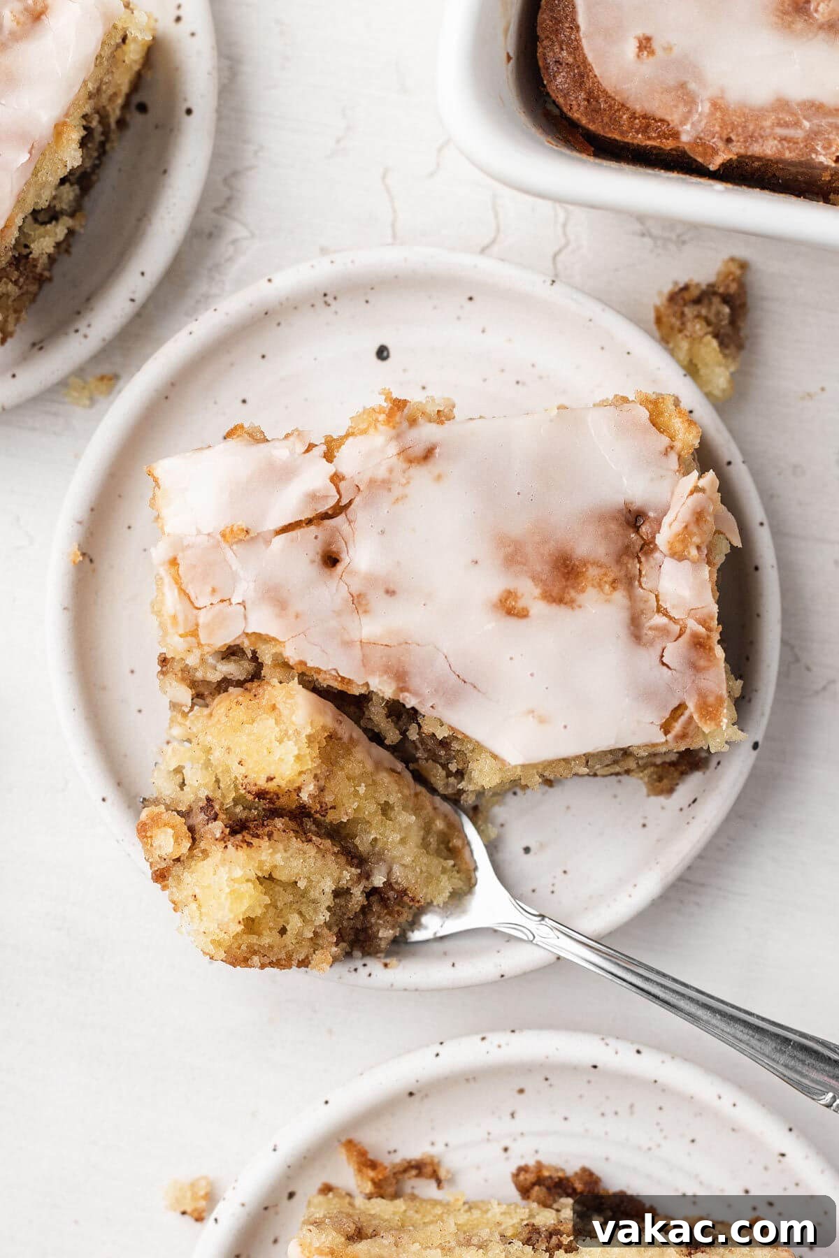 Cinnamon Swirl Honey Bun Delight 9 An overhead view of a slice of iced honey bun cake. A fork has speared a bite of cake and rests on its side on the plate.