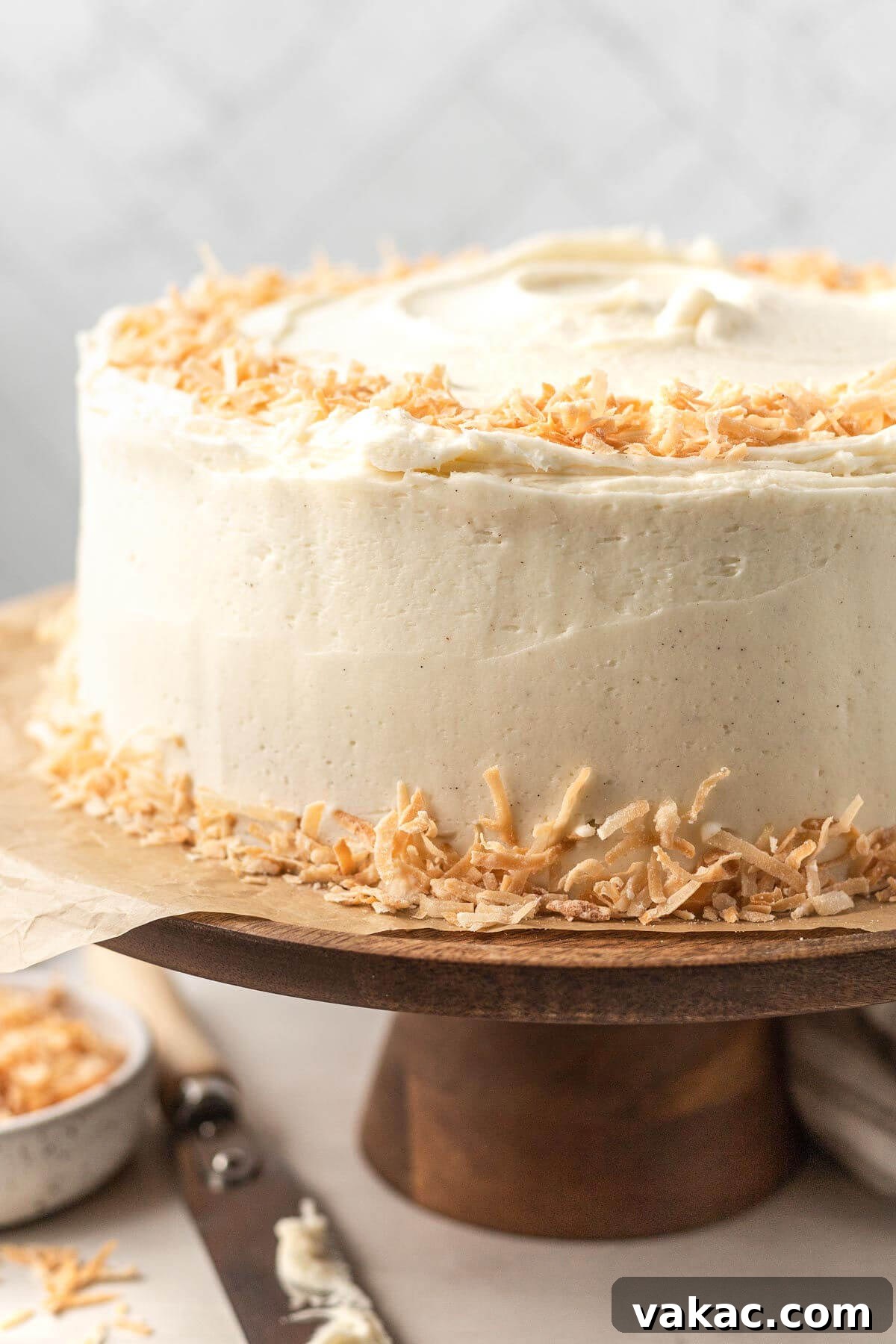 Fluffy Coconut Cloud Cake 2 A coconut cake with coconut buttercream frosting and toasted coconut on a wooden cake stand.