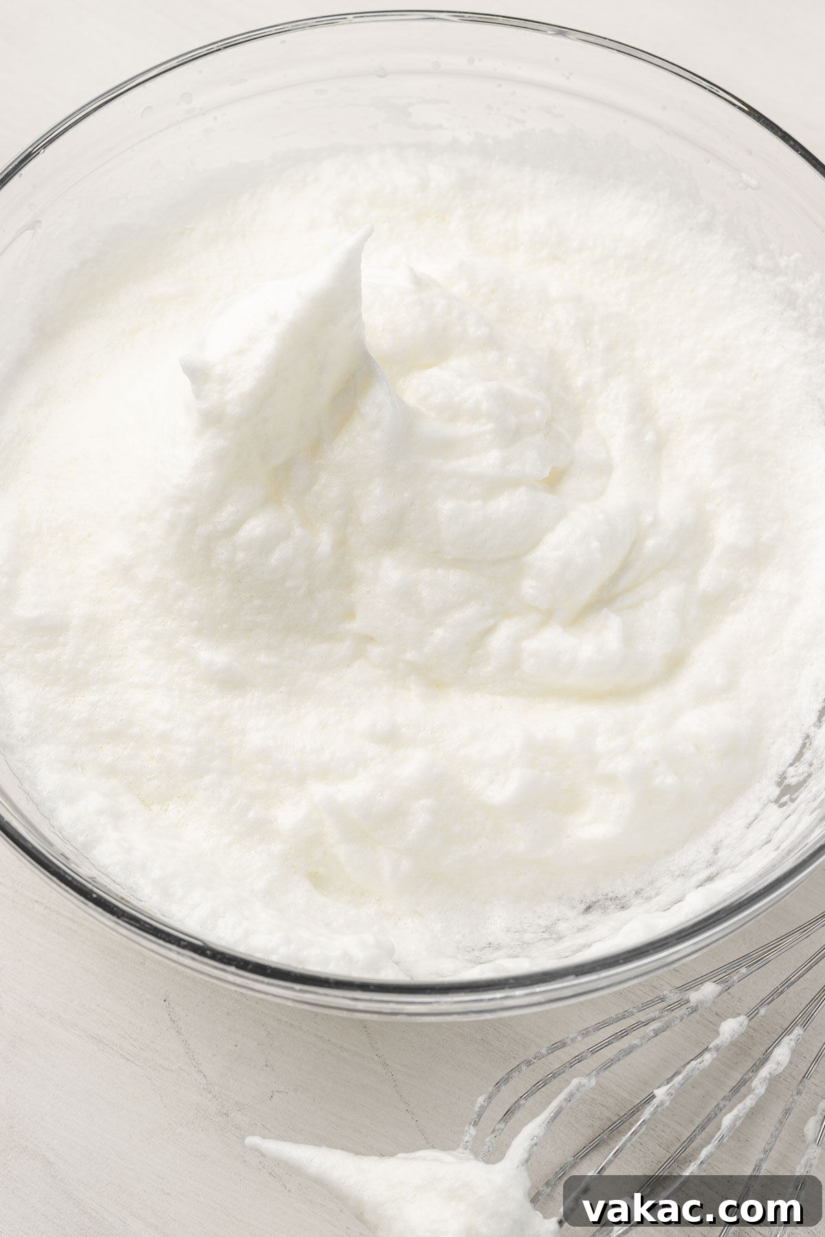 A glass mixing bowl with egg whites that have been beaten to stiff peaks.