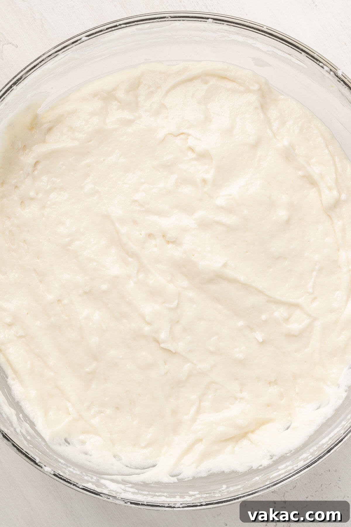 A glass mixing bowl with coconut cake batter in it.