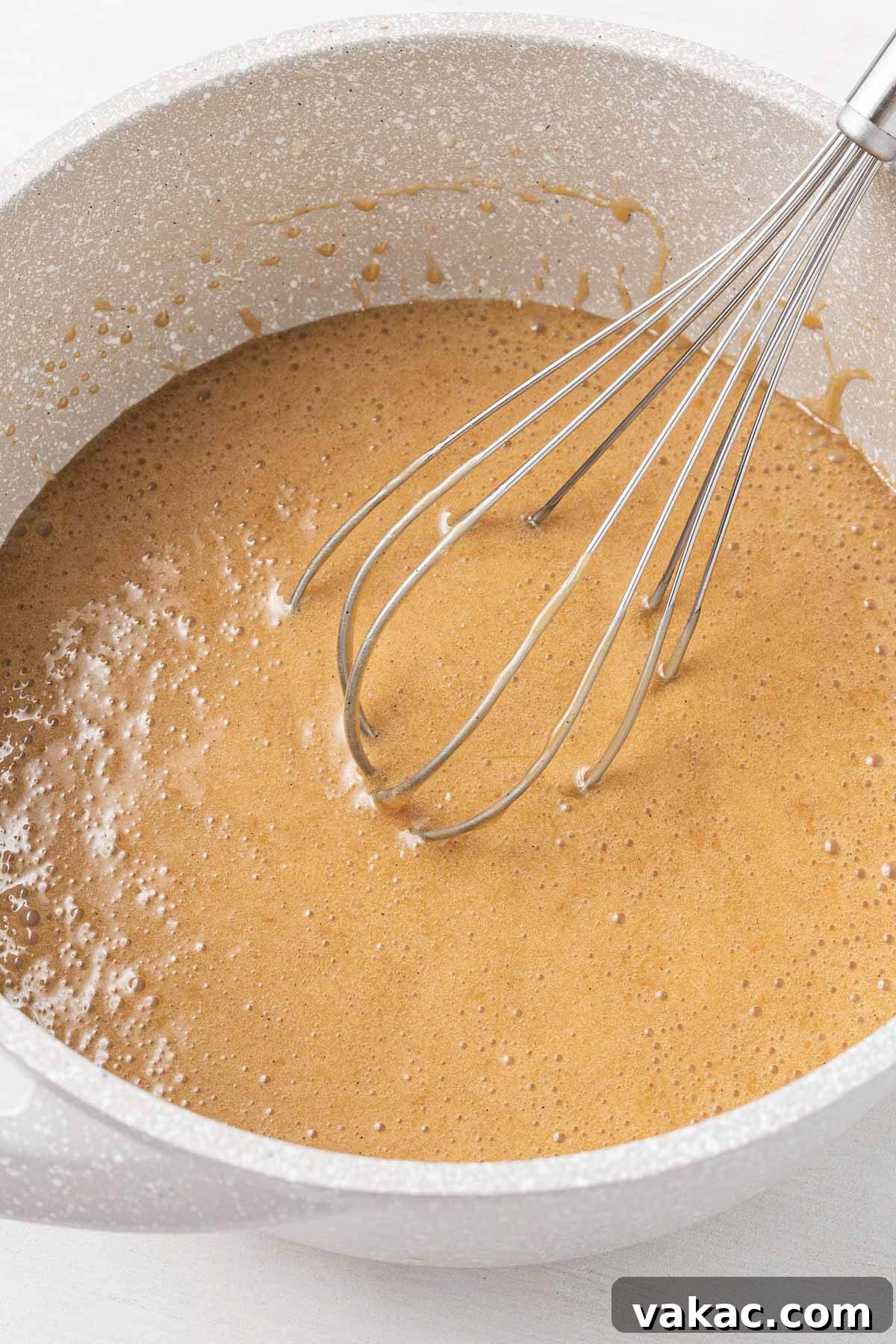 Golden Caramel Popcorn 4 Caramel sauce in a white mixing bowl with a whisk.