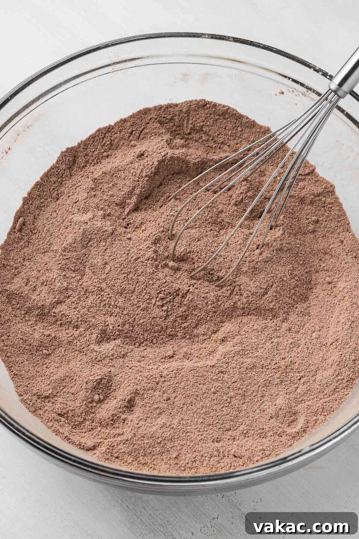 Overhead view of the dry ingredients for a chocolate cake in a glass mixing bowl with a whisk.