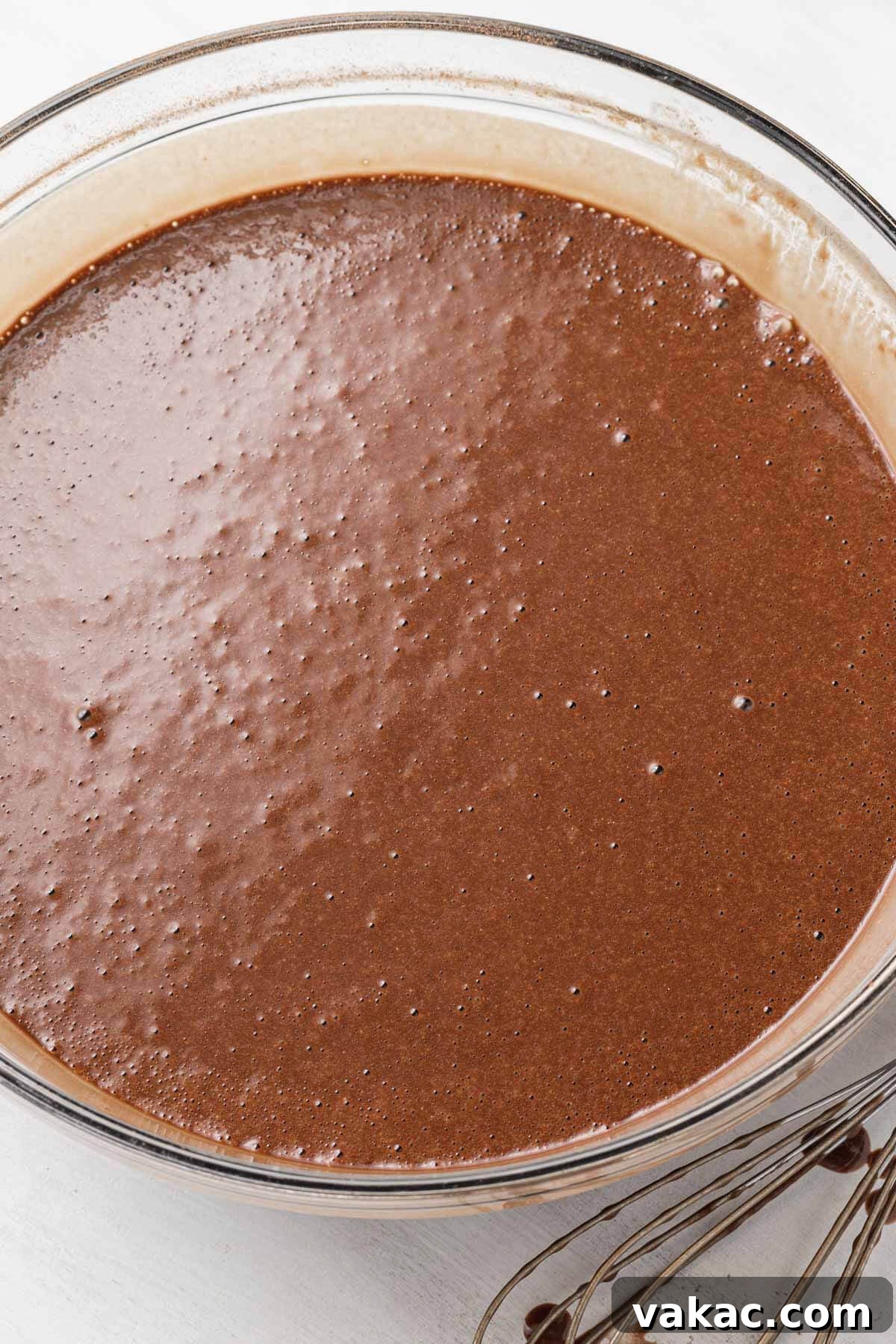 An overhead view of chocolate cake batter in a glass mixing bowl.