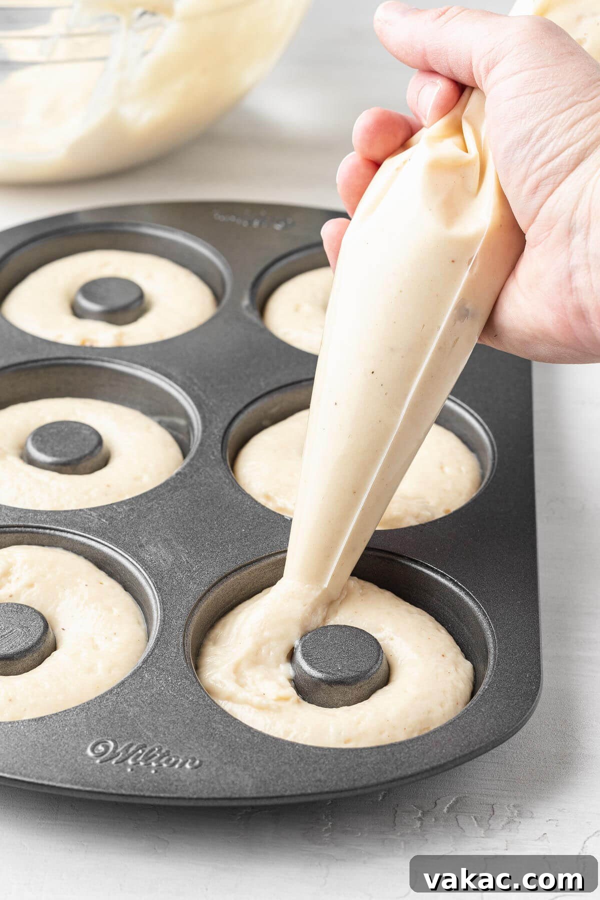 Donut batter being piped into a donut pan.