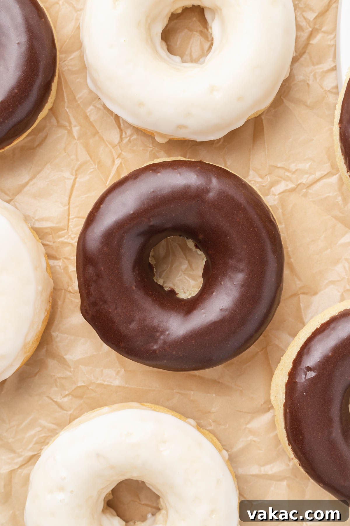 An overhead view of baked donuts with icing on a piece of parchment paper. 