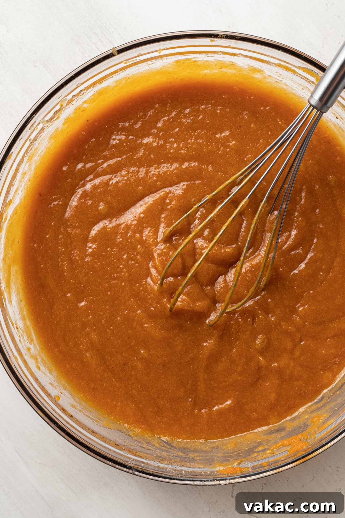 An overhead view of smooth, golden pumpkin bar batter expertly mixed in a clear glass mixing bowl, showcasing its rich texture.