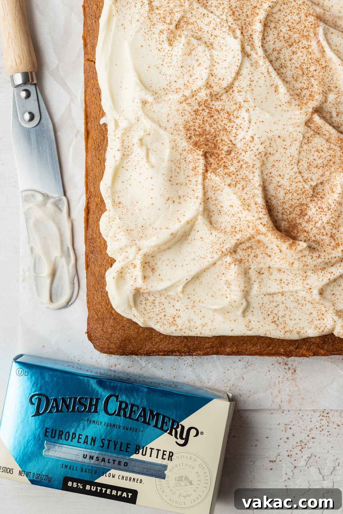 Autumn Spiced Pumpkin Bars 8 An overhead shot of a freshly baked, unsliced pan of frosted pumpkin bars, with an offset spatula and a package of Danish Creamery butter suggesting its rich flavor.