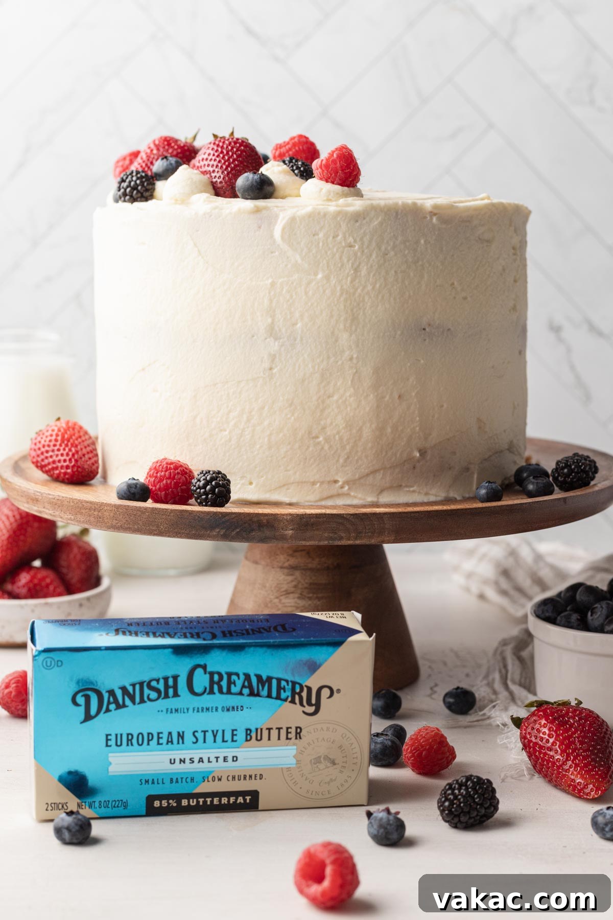 Berry Chantilly Delight 2 A beautifully decorated Chantilly cake on a wooden cake stand, with a package of premium Danish Creamery butter positioned elegantly in front.