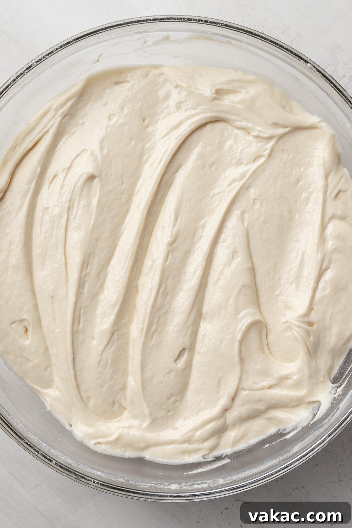 An overhead perspective of velvety vanilla cake batter, perfectly mixed and ready for baking in a pristine glass mixing bowl, showcasing its smooth texture.