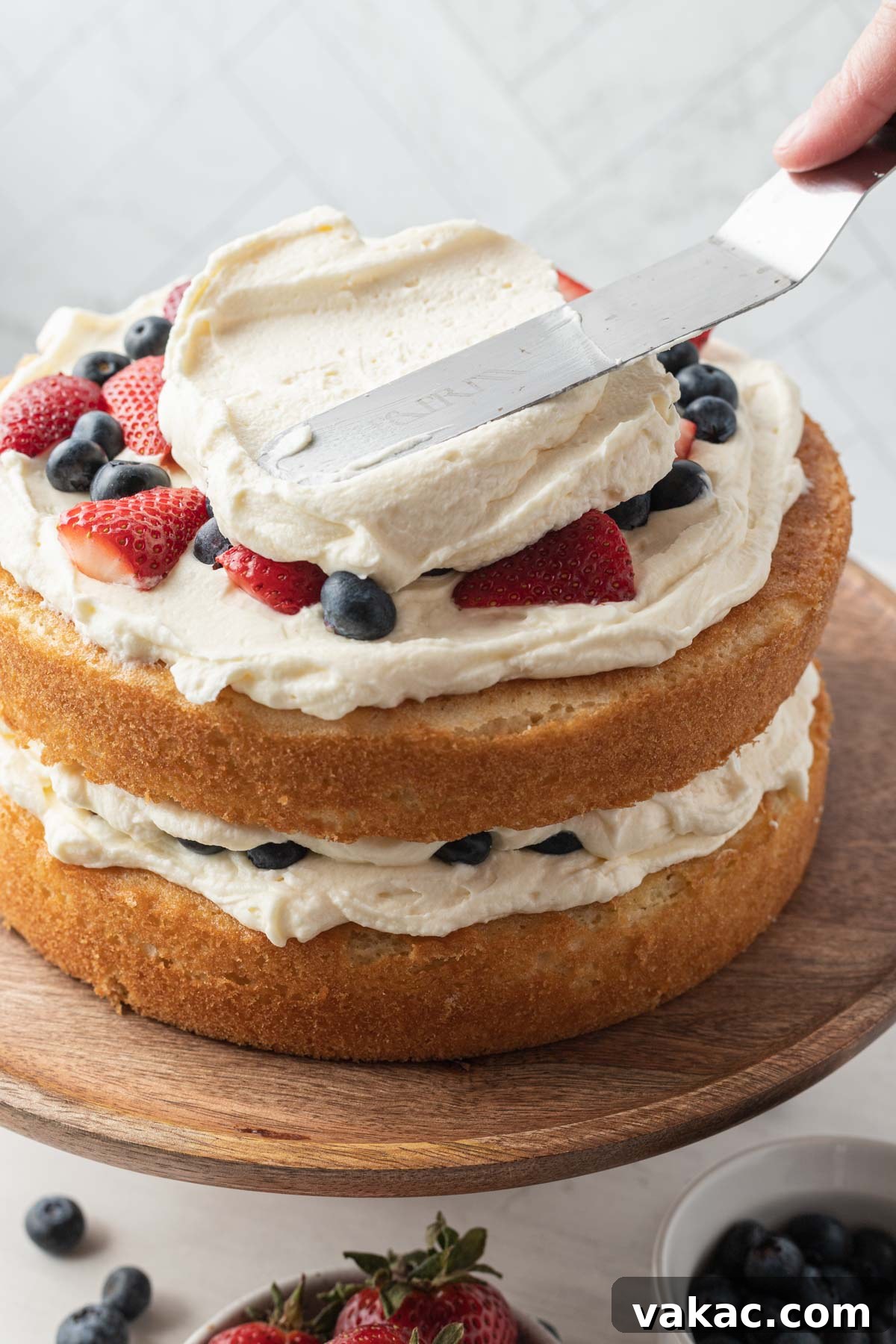 A process shot demonstrating the initial stages of frosting a Chantilly berry cake, with a smooth layer of cream applied to the first cake layer.