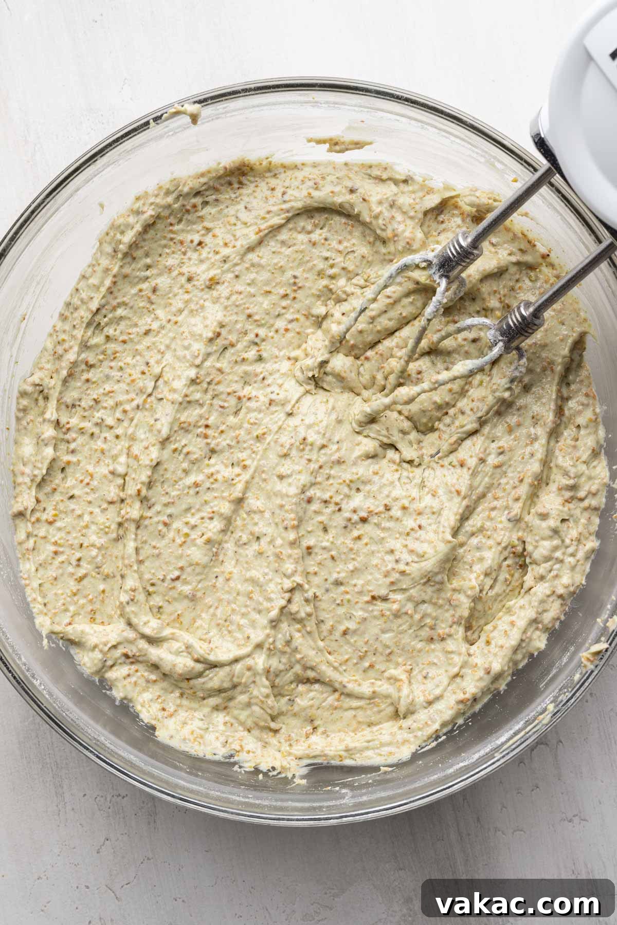 An overhead view of pistachio cake batter with electric beaters in a glass mixing bowl.