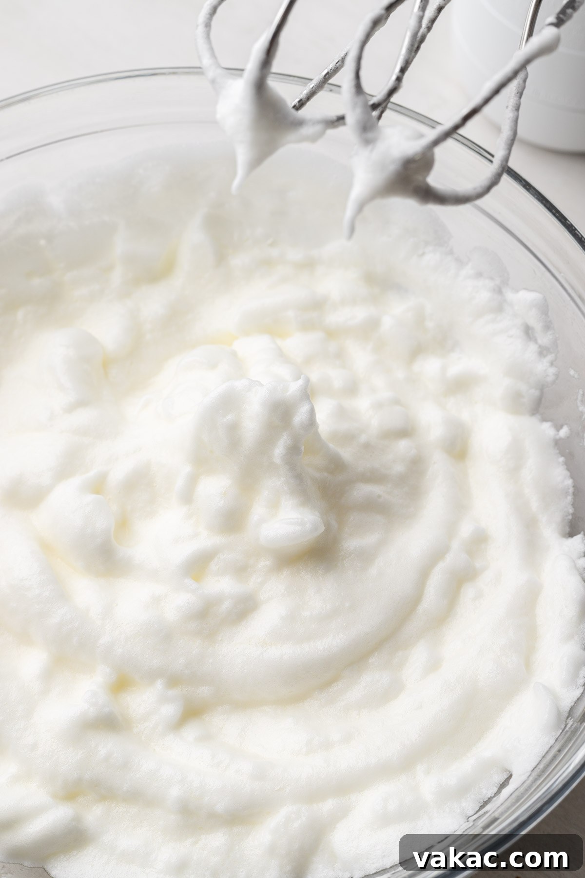 Whipped egg whites with electric beaters in a glass bowl.